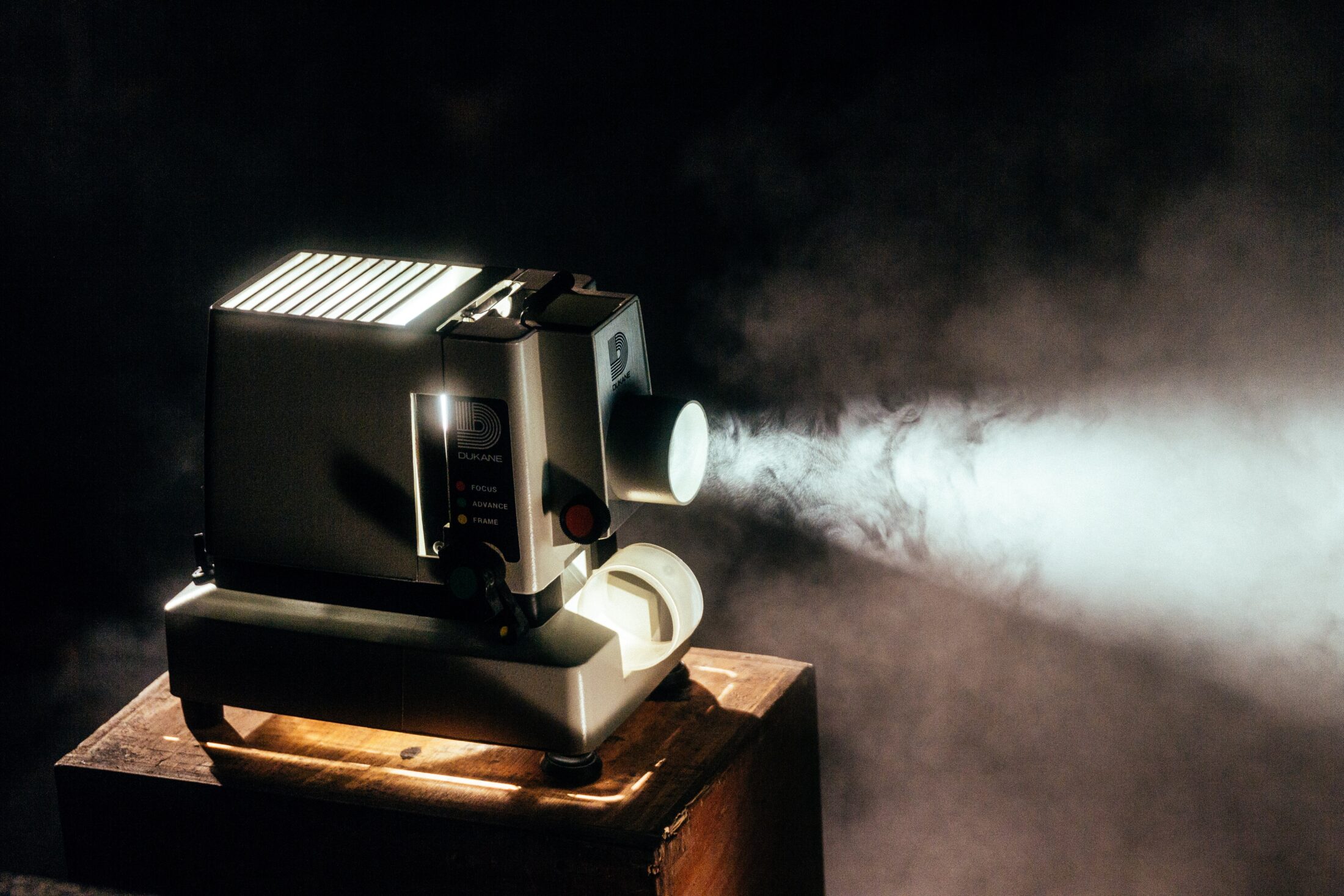 High res image of a old movie theatre projector, with light shining through the lens with white smoke.